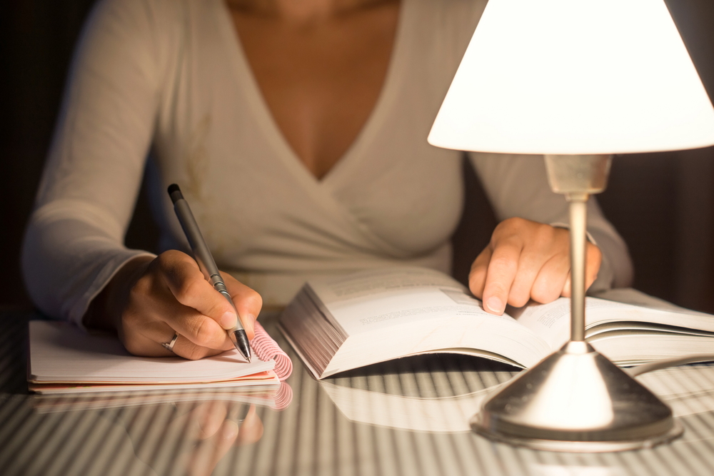 woman writing in notebook next to large book