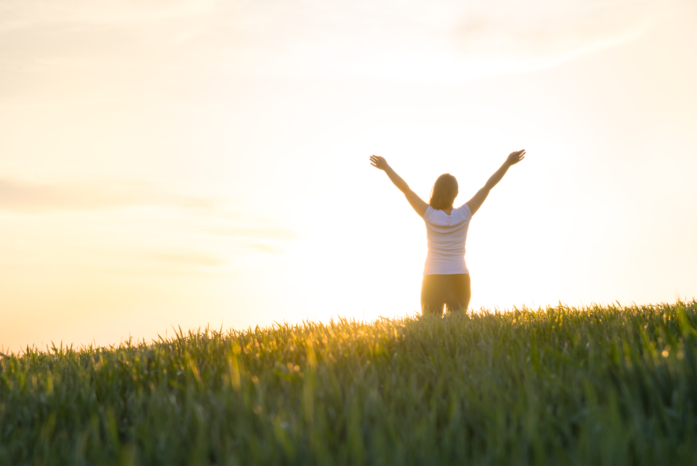 woman extending arms in field at sunset